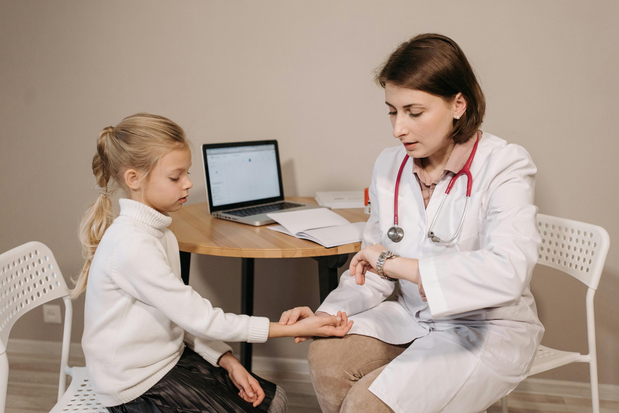 A doctor examines a young girl during a pediatric consultation in an indoor clinic setting.